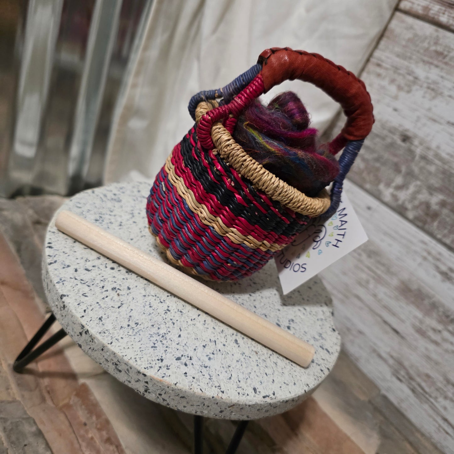 Colorful woven basket on a speckled stone surface with a wooden stick
